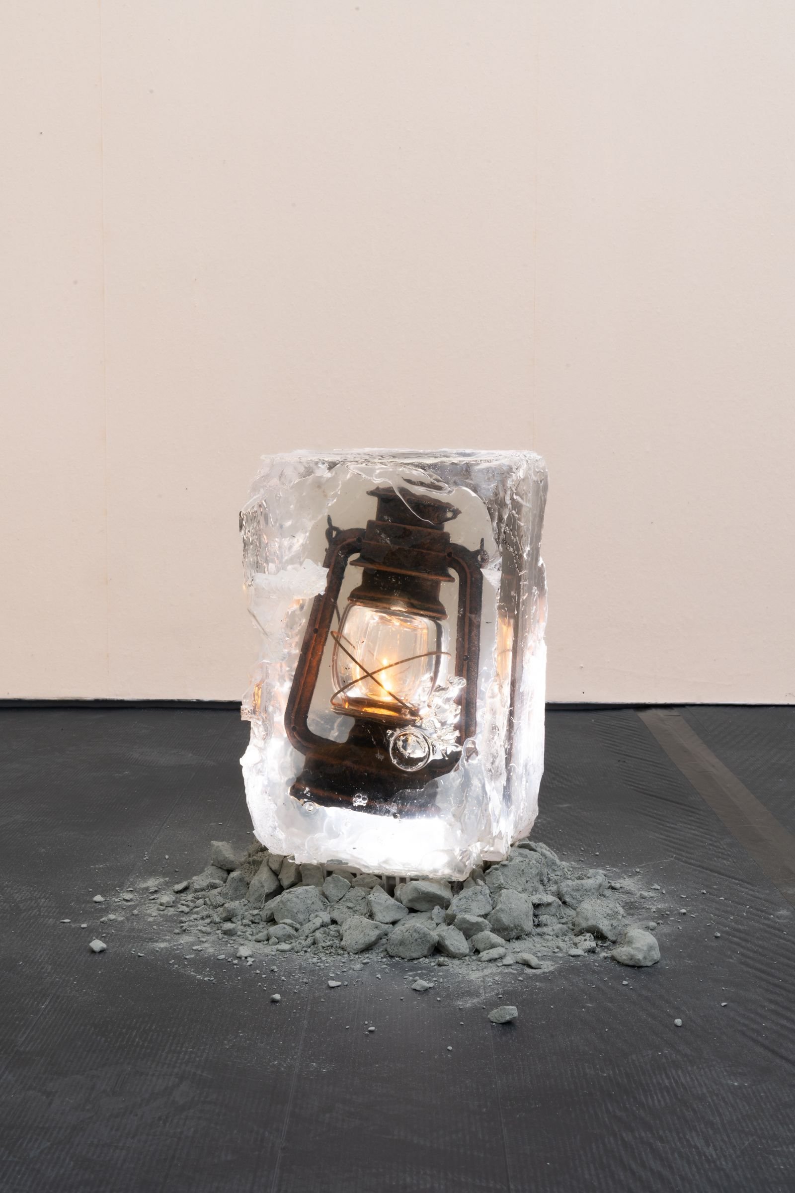 A lantern encased in ice sits on gravel.