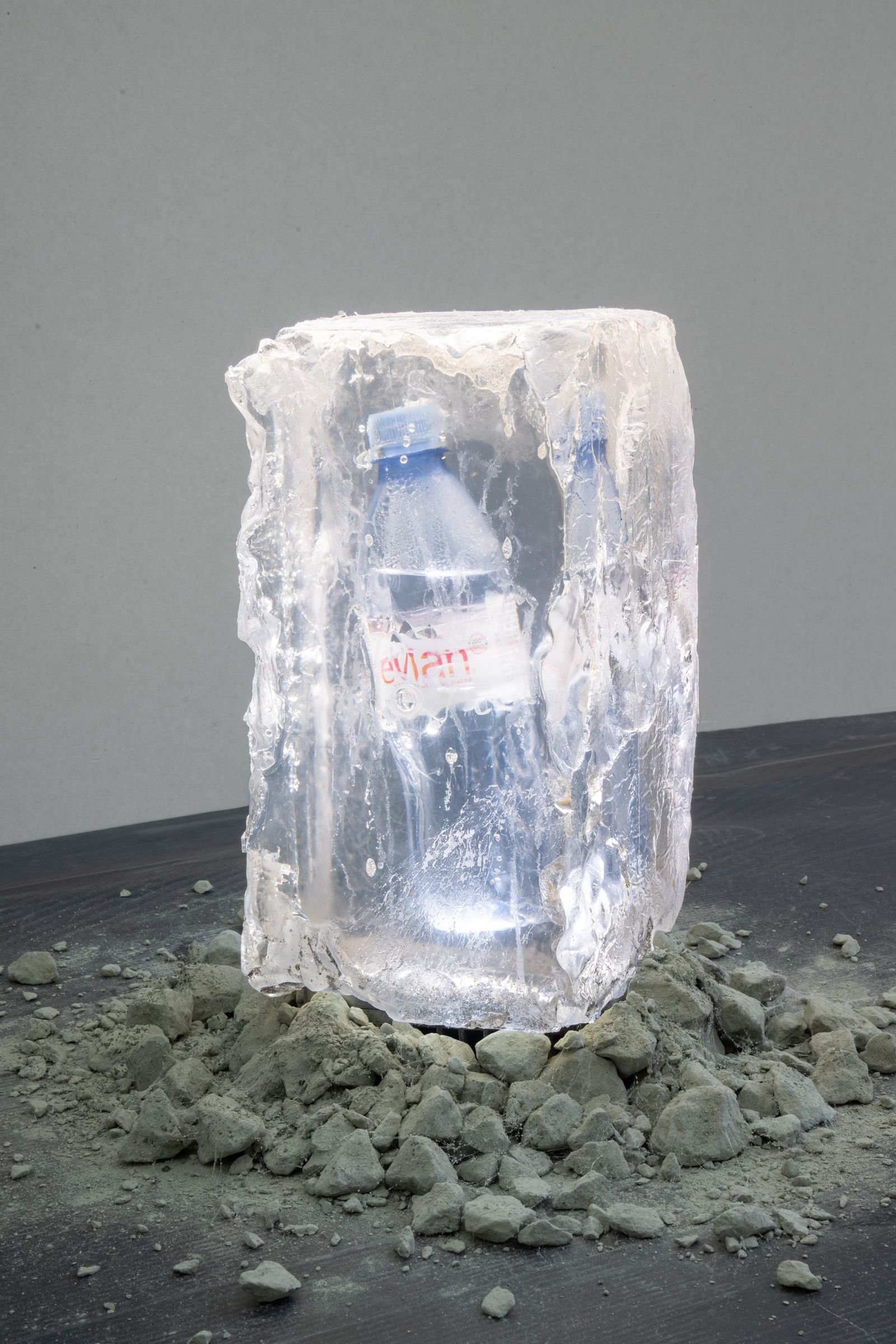 A water bottle encased in ince sits on gravel.