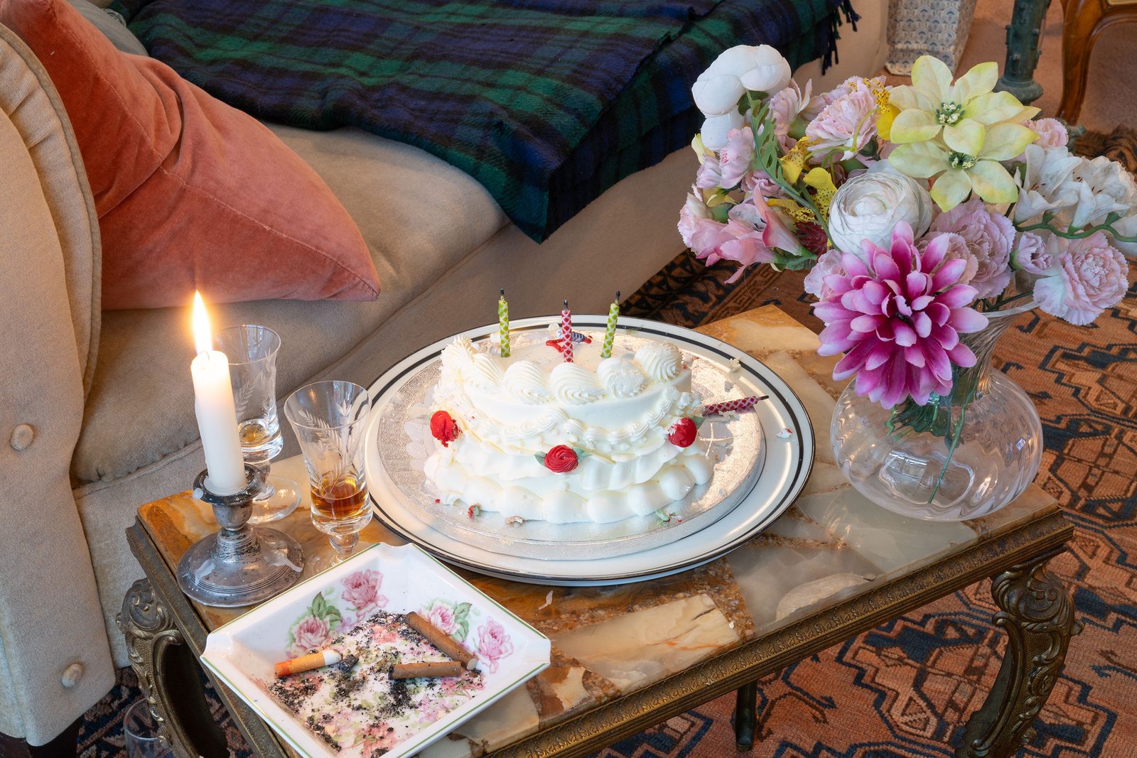 coffee table with half eaten birthday cake, ashtray and plastic flowers